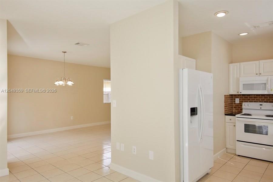A kitchen with white cabinets and appliances opens into a dining area with tile flooring — HOMESTEAD, FL