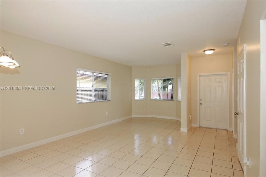 An empty room features beige walls, light-colored tile flooring, and a white front door — HOMESTEAD, FL