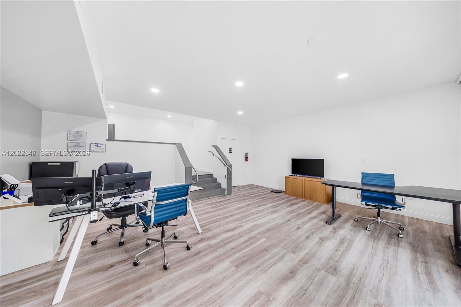 An office space features light wood-look flooring, white walls, two desks, and a staircase — 8009 NW 29th St # 8009, Doral FL 33122, DORAL, FL