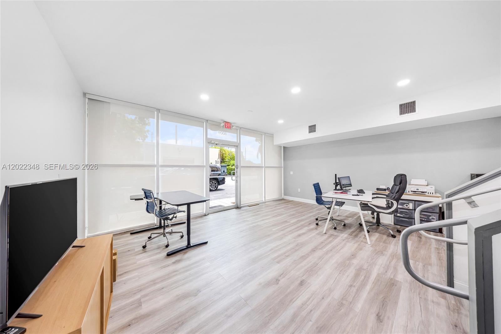 An office space features light wood-look flooring, white walls, large windows, and two desks — 8009 NW 29th St # 8009, Doral FL 33122, DORAL, FL