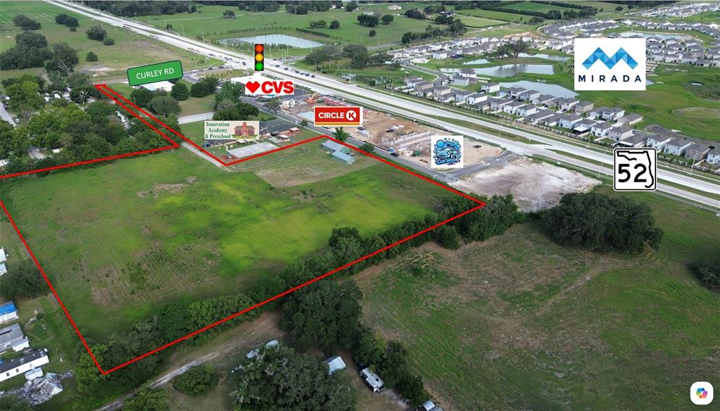 An aerial view shows a large, undeveloped grassy lot outlined in red near commercial businesses — 0 BOYS VILLAGE LANE, SAN ANTONIO, FL