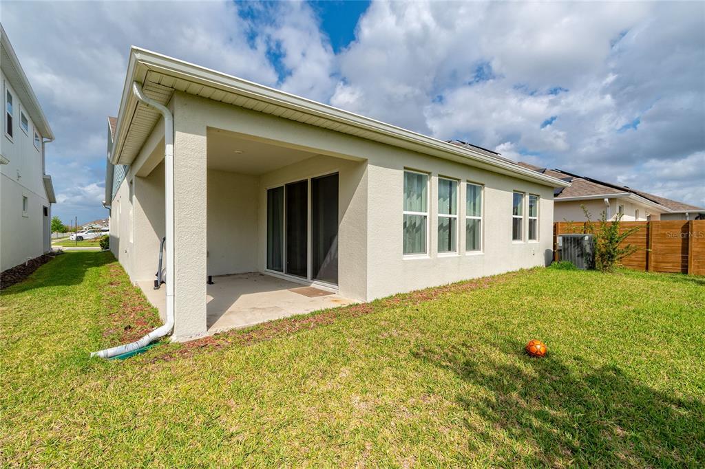 The exterior of a house features a covered patio, sliding glass doors, and a grassy backyard — 14815 MILFOIL AVENUE, ORLANDO, FL