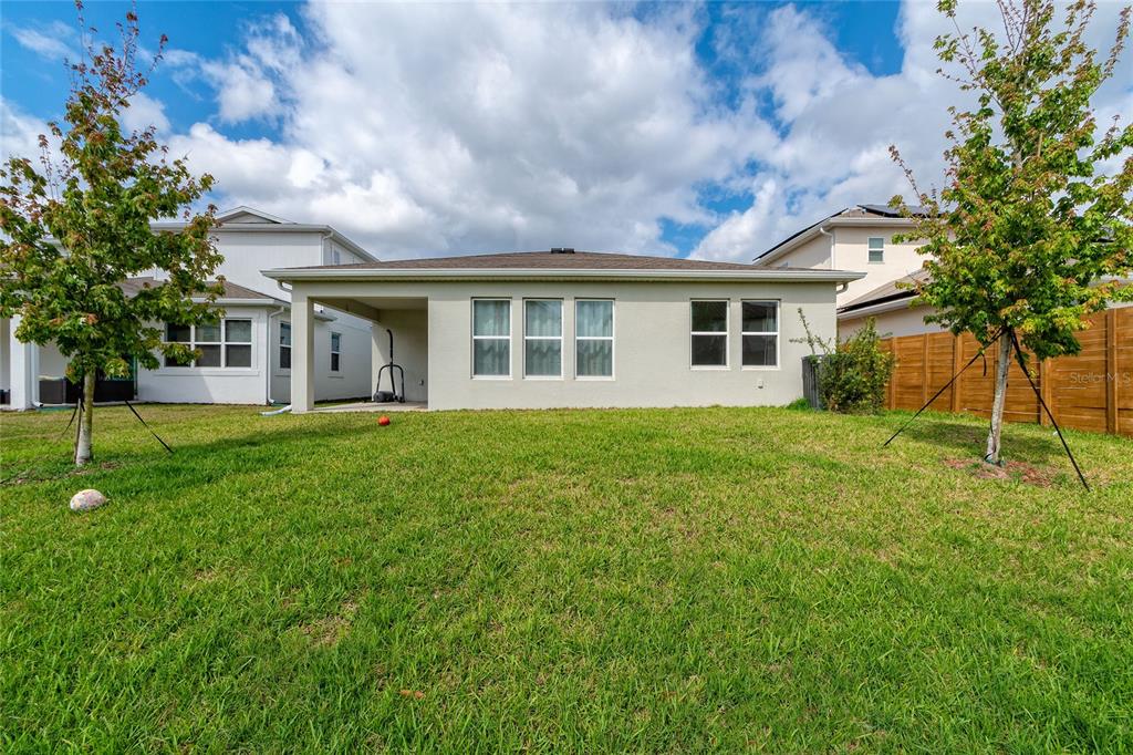 The exterior rear view of a single-story house features a covered patio and grassy yard — 14815 MILFOIL AVENUE, ORLANDO, FL