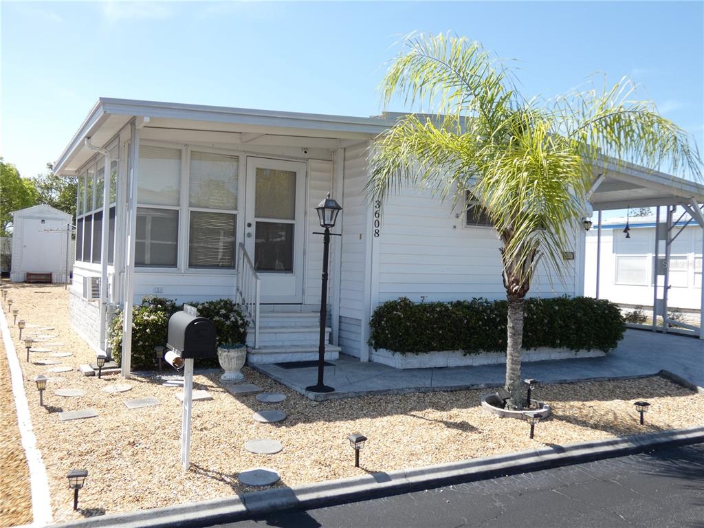 A white mobile home with a screened porch, gravel yard, and a palm tree — 3608 TIKI DRIVE, HOLIDAY, FL