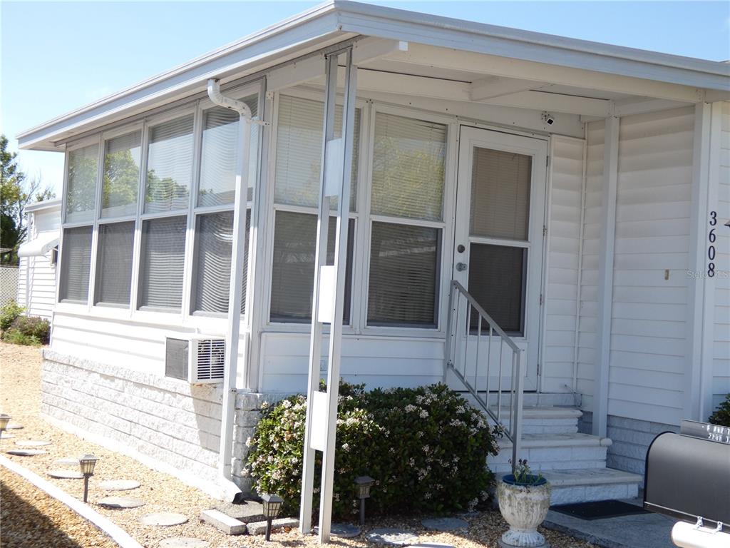 The exterior of a white mobile home features a screened-in porch and a front entrance — 3608 TIKI DRIVE, HOLIDAY, FL