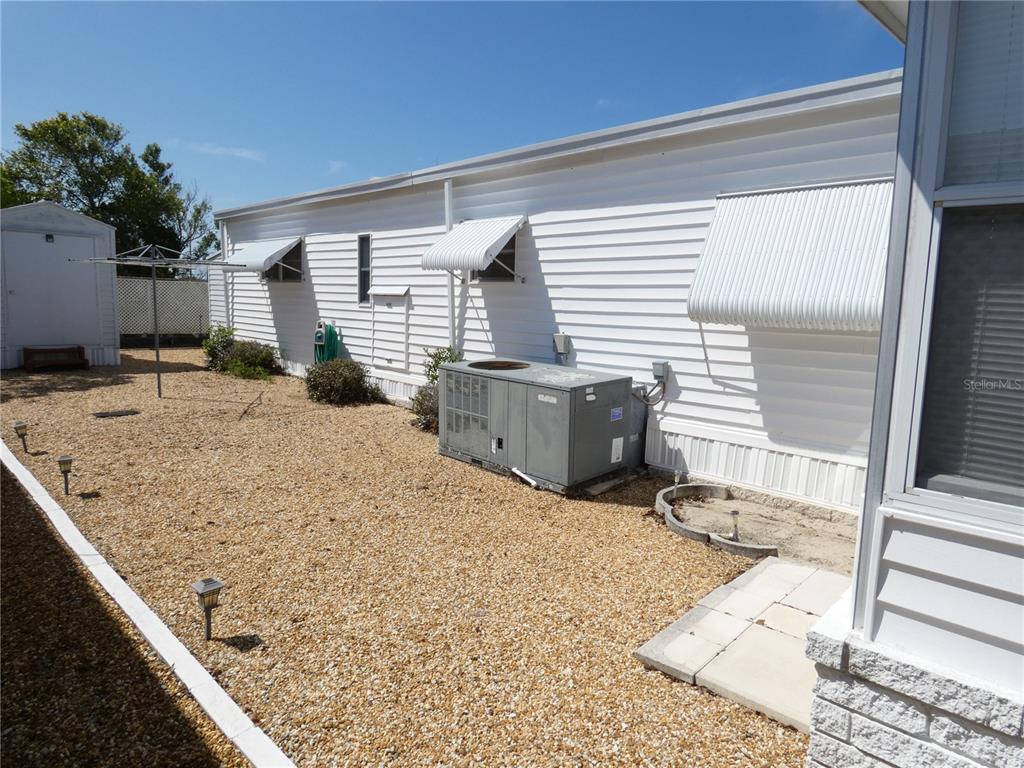 The exterior of a mobile home features white siding, metal awnings, and a gravel yard — 3608 TIKI DRIVE, HOLIDAY, FL