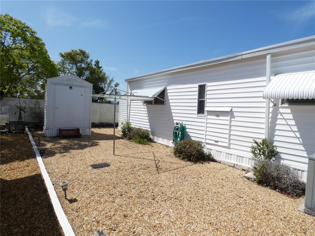 A white mobile home exterior with a gravel yard, storage shed, and clothesline — 3608 TIKI DRIVE, HOLIDAY, FL