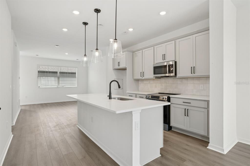 A modern kitchen features light gray cabinets, white countertops, a center island, and wood-look flooring — 17398 SWEET MORO DRIVE, WINTER GARDEN, FL