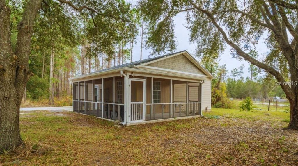 A small, light-colored house with a large screened-in porch sits among trees — 19751 COUNTY ROAD 33, GROVELAND, FL