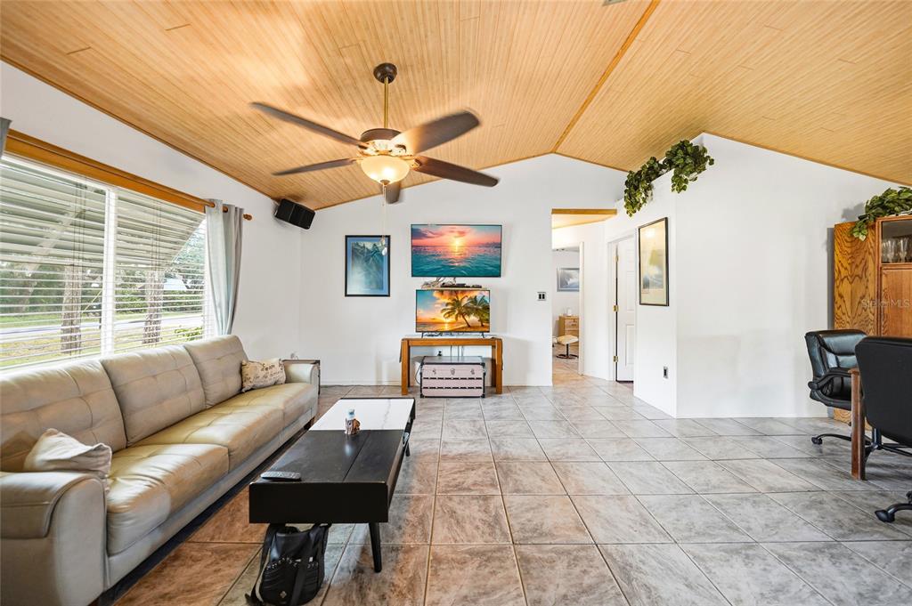 A living room features a vaulted wood-paneled ceiling, tile flooring, a sofa, and a television — 2631 FIESTA DRIVE, VENICE, FL