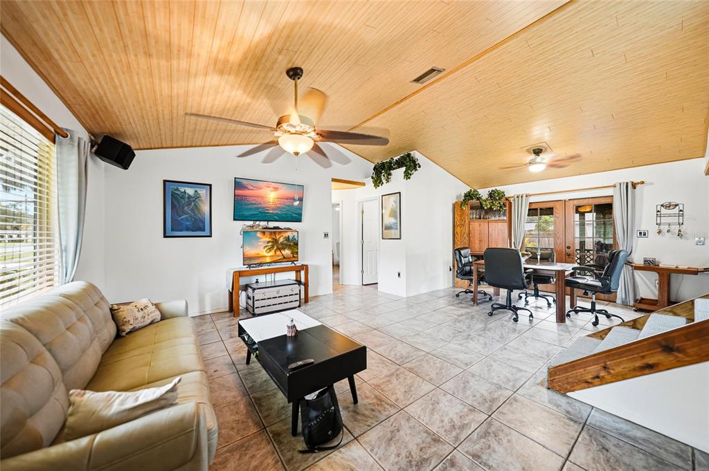 A living room with a wood-paneled vaulted ceiling, tile floors, and a dining area — 2631 FIESTA DRIVE, VENICE, FL