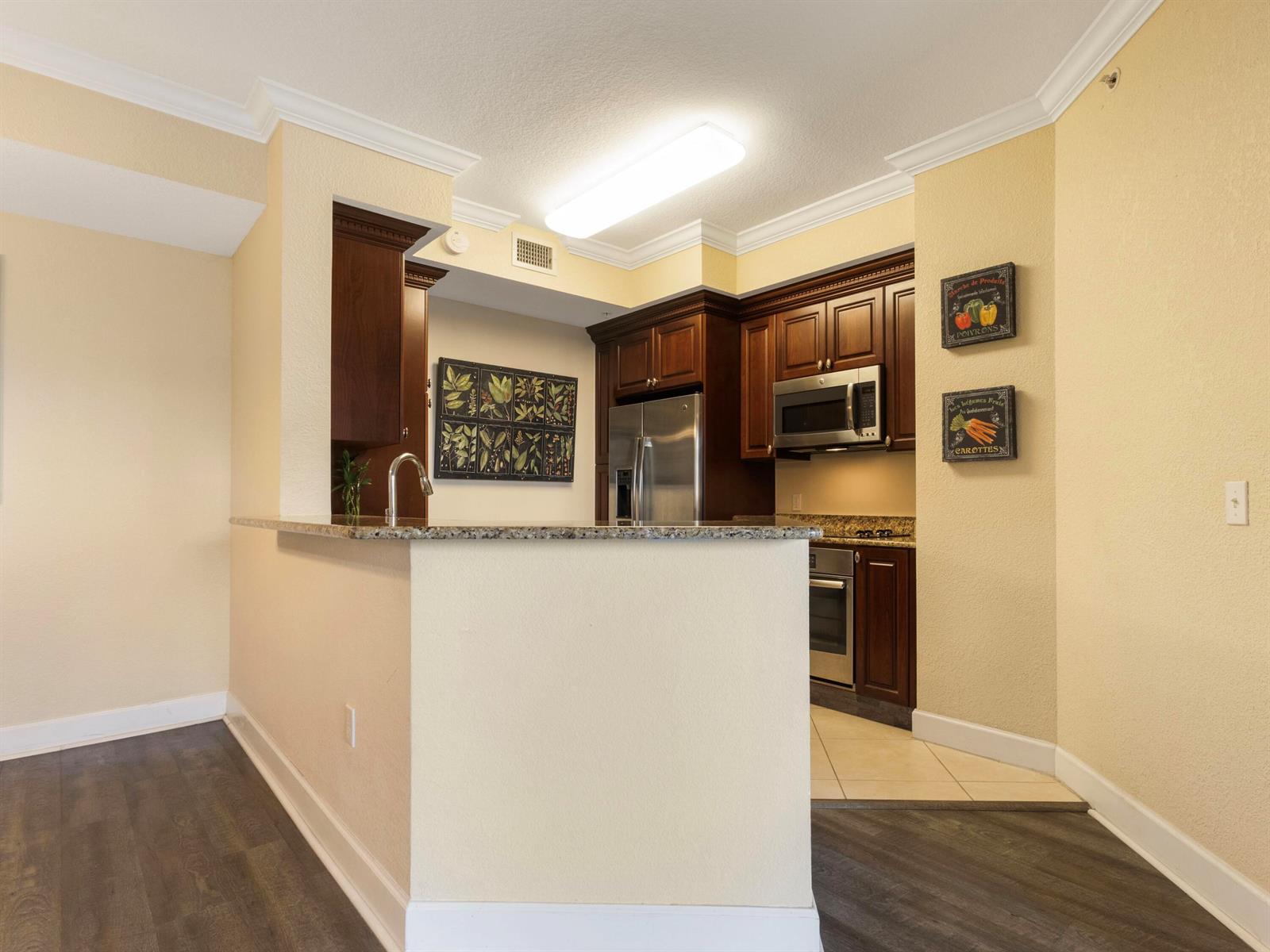 A kitchen features dark wood cabinets, granite countertops, stainless steel appliances, and light-colored walls — 1690 Renaissance Commons Boulevard # 1412, Boynton Beach FL 33426, BOYNTON BEACH, FL