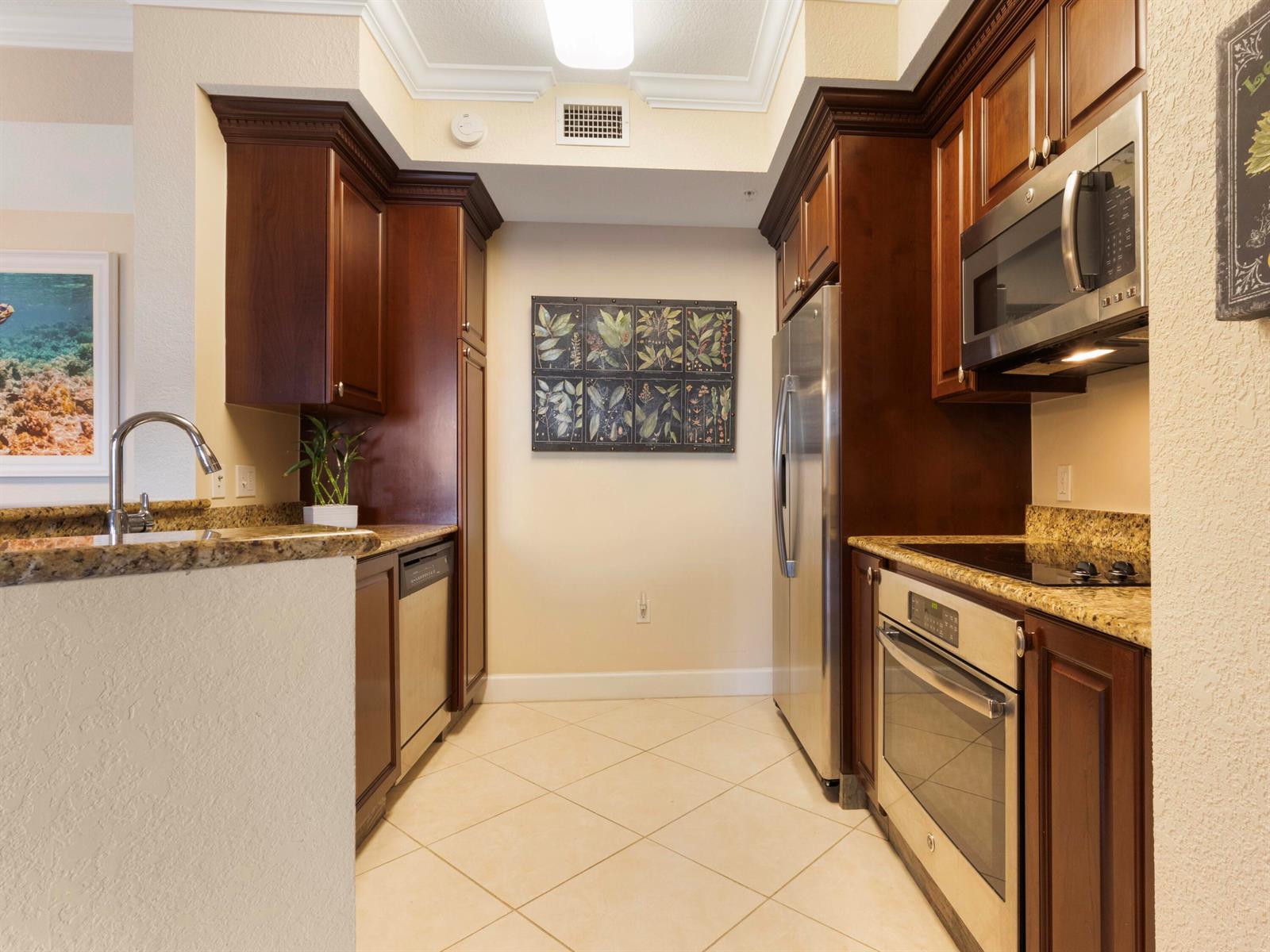 A galley kitchen features dark wood cabinets, granite countertops, and stainless steel appliances — 1690 Renaissance Commons Boulevard # 1412, Boynton Beach FL 33426, BOYNTON BEACH, FL