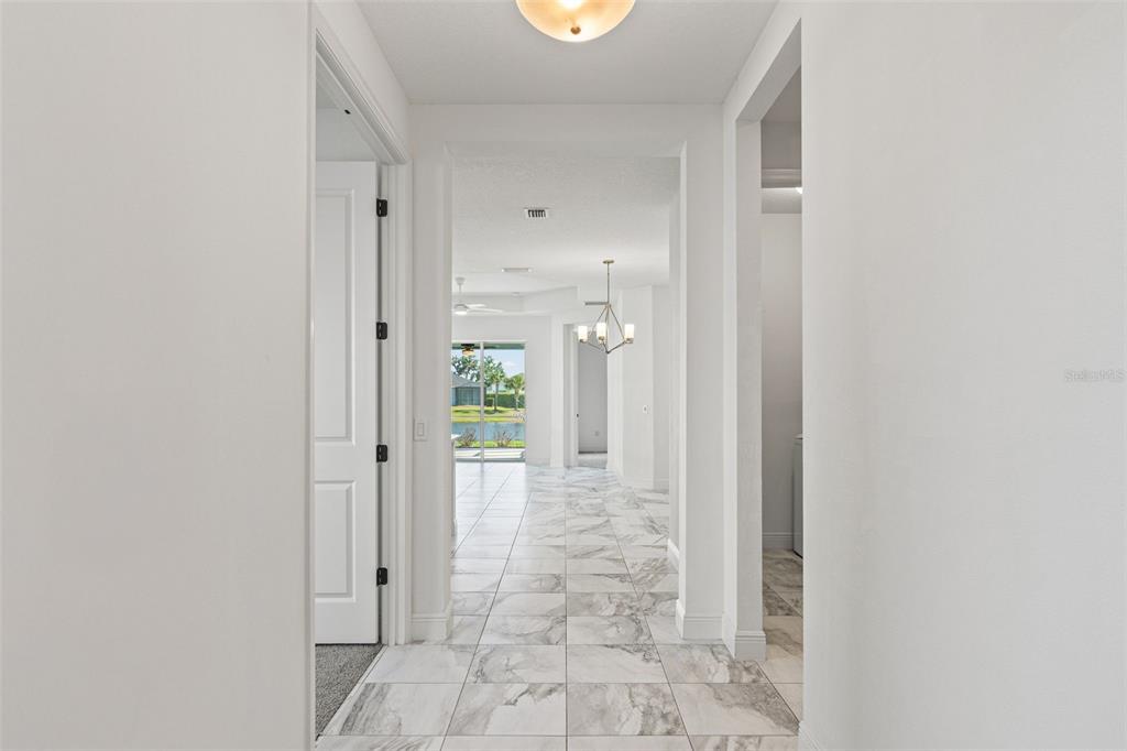 A hallway with white walls and marble-patterned tile flooring leads to a view of water — 14632 BAREFOOT LANE, PARRISH, FL