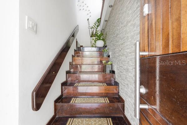 A wooden staircase with patterned treads leads upward beside a textured stone wall — #9 MANUEL POLOP SOLER, UTUADO, PR