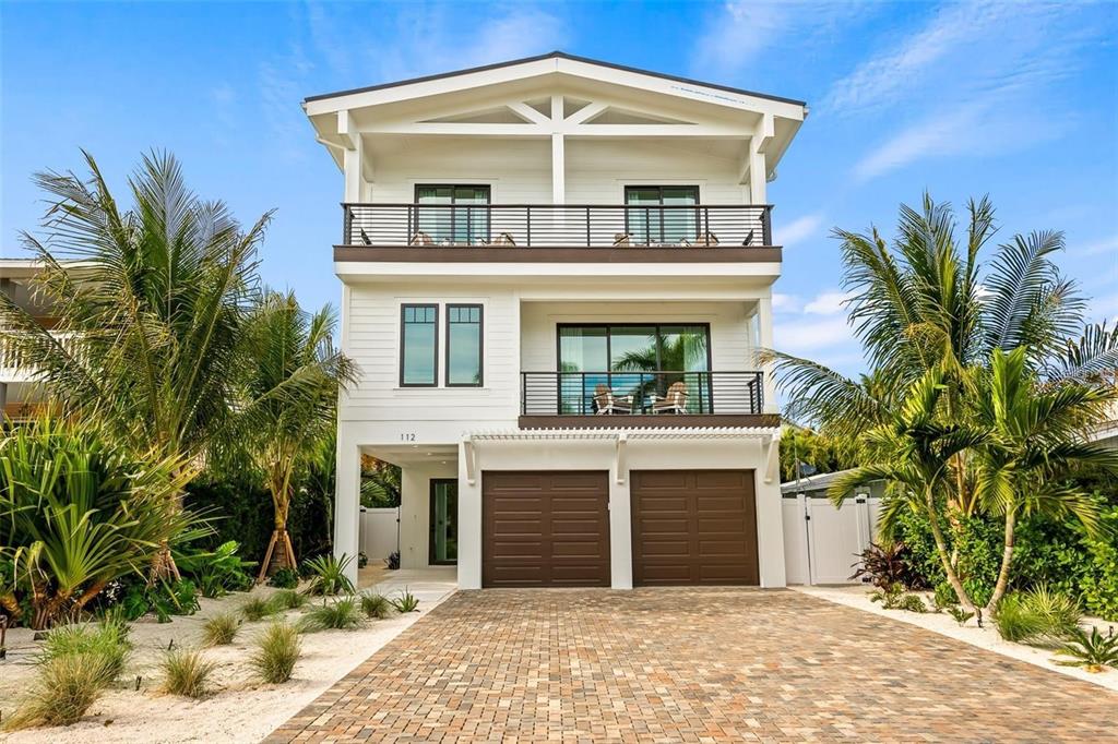 A three-story white house with two garage doors and balconies sits on a paved driveway — 112 MAPLE AVENUE, ANNA MARIA, FL