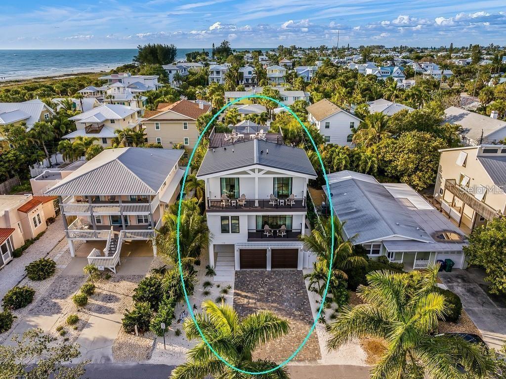 An aerial view of a three-story coastal home with a rooftop deck and paved driveway — 112 MAPLE AVENUE, ANNA MARIA, FL
