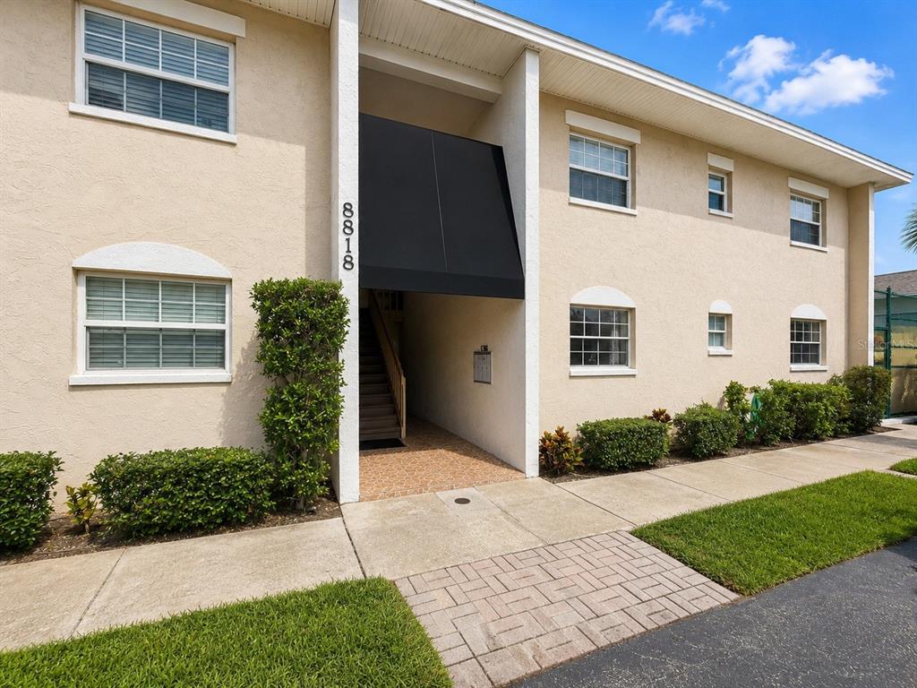 A two-story apartment building exterior features tan stucco walls, a black awning, and a walkway — 8818 BAY POINTE DRIVE UNIT 108, TAMPA, FL