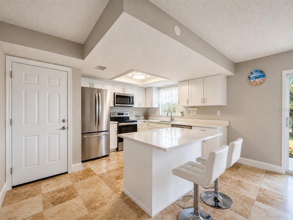 An open-concept living area features light tile flooring, a kitchen with white cabinetry, and waterfront views — 8818 BAY POINTE DRIVE UNIT 108, TAMPA, FL