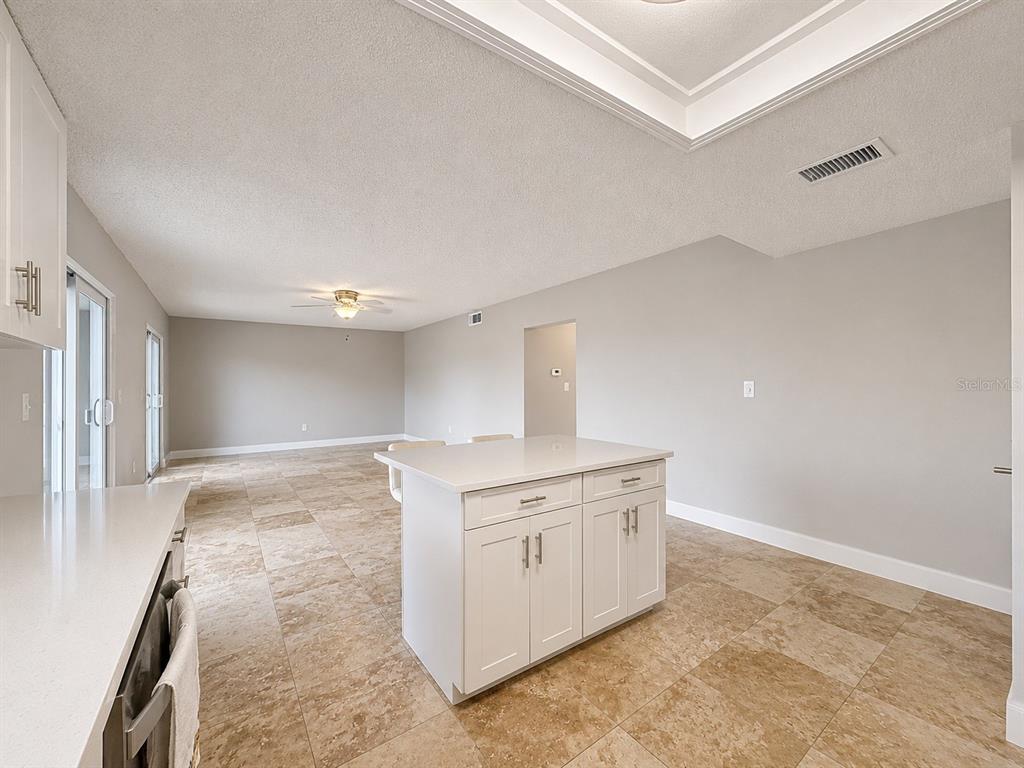 A kitchen features white cabinets, stainless steel appliances, a central island, and tiled flooring — 8818 BAY POINTE DRIVE UNIT 108, TAMPA, FL