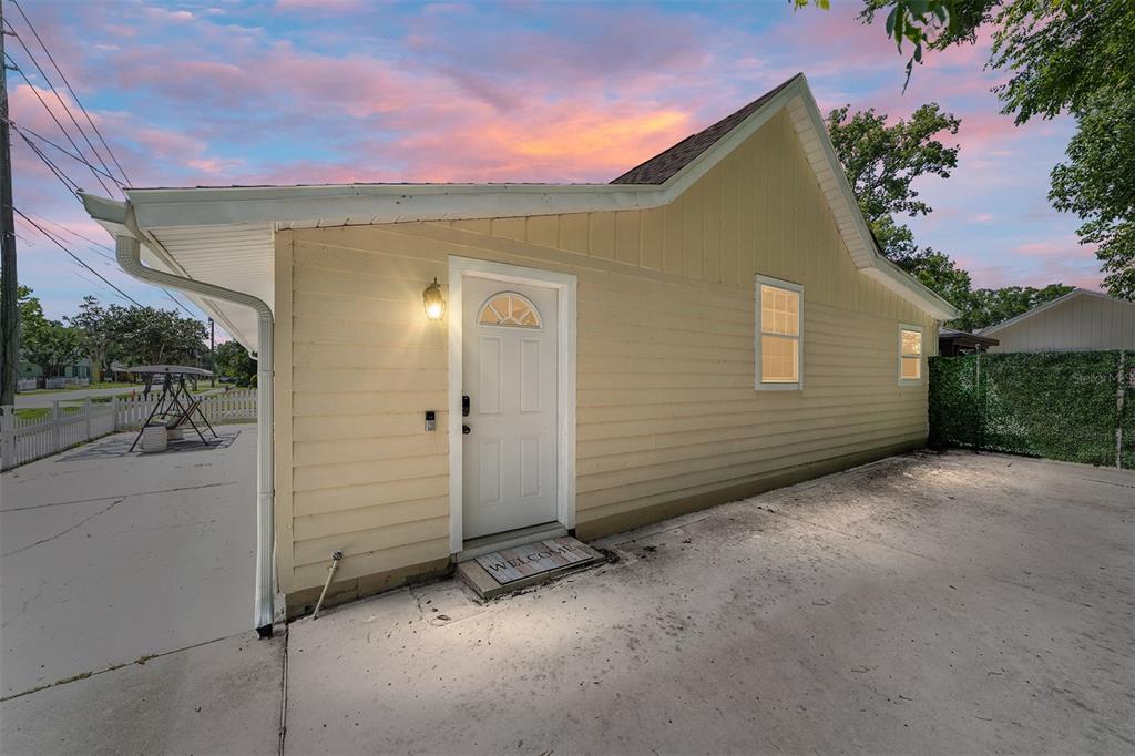 A yellow house exterior features a white door, a concrete patio, and a sunset sky — 20693 WALNUT STREET, DUNNELLON, FL
