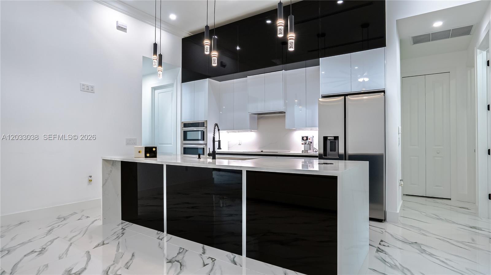 A modern kitchen features a black and white island, glossy cabinetry, and marble-patterned tile flooring — 2565 28th Ave Se, Naples FL 34117, NAPLES, FL