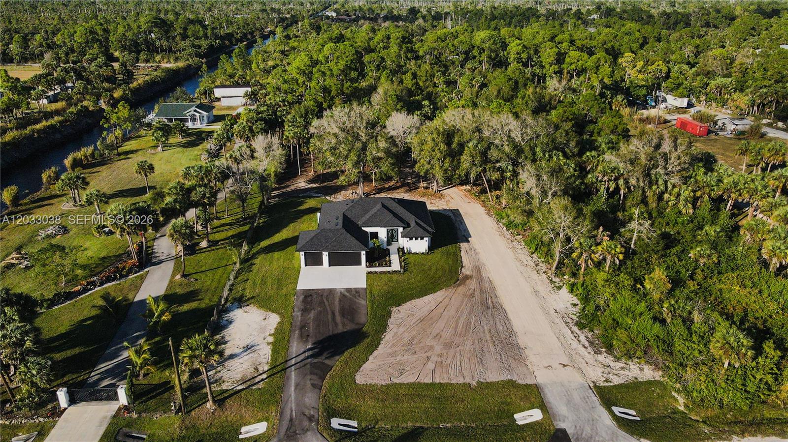 An aerial view shows a modern house with a dark roof and driveway amidst trees — 2565 28th Ave Se, Naples FL 34117, NAPLES, FL