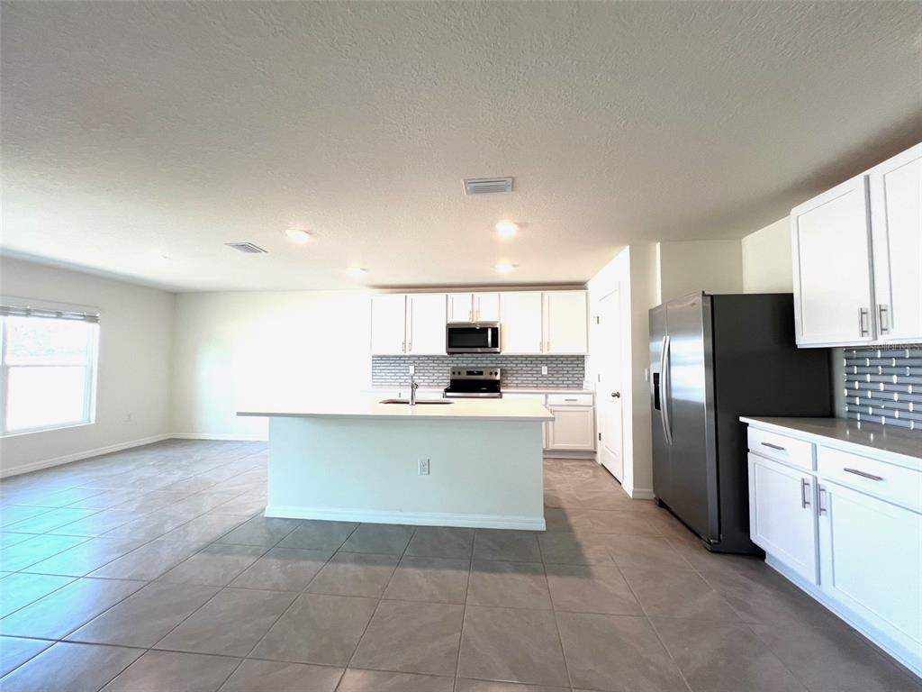 A kitchen features white cabinets, a central island, stainless steel appliances, and gray tile flooring — 6527 SE 1ST LOOP, OCALA, FL