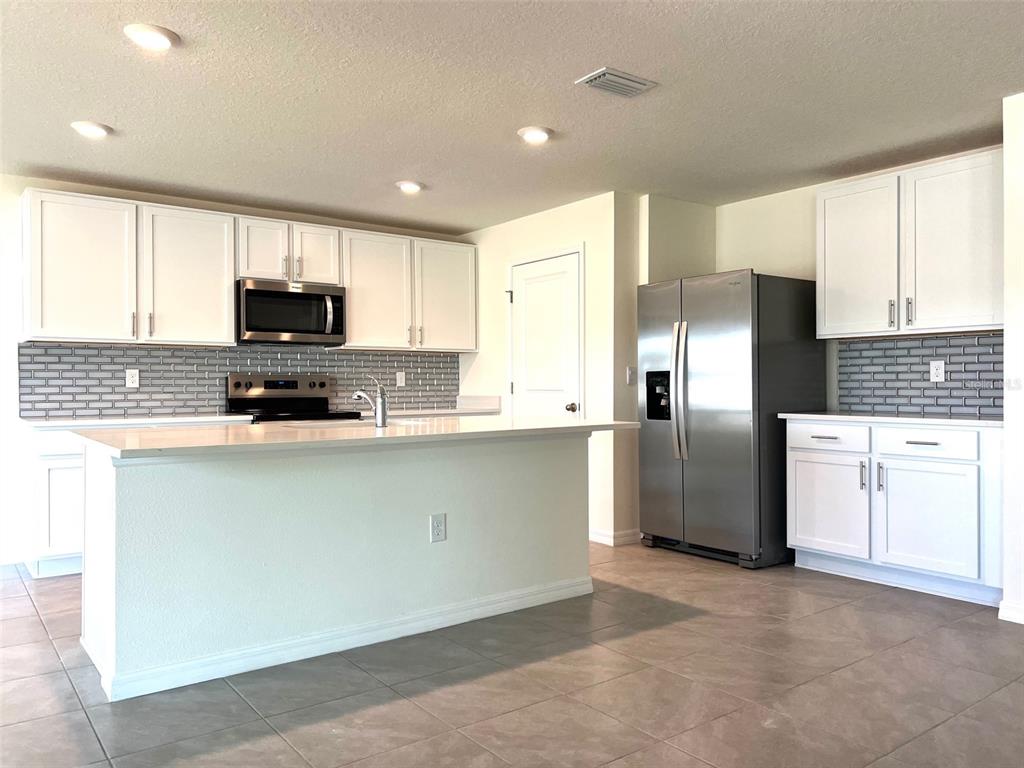 A kitchen features white cabinets, stainless steel appliances, a gray tile backsplash, and a central island — 6527 SE 1ST LOOP, OCALA, FL