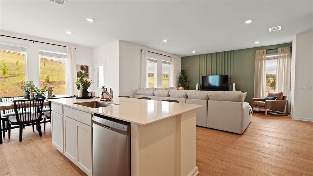 An open-concept kitchen and living area features a central island, light flooring, and green accent wall — 6052 BALANCE WAY, CLERMONT, FL