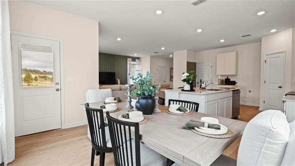 A dining area with a wooden table and black chairs opens to a kitchen island — 6052 BALANCE WAY, CLERMONT, FL