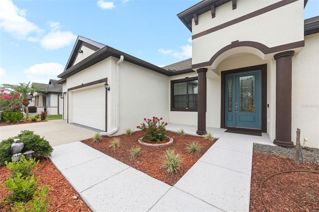 A single-story house exterior features a white stucco facade, a blue front door, and landscaping — 11026 BRAHMAN RANCH CIRCLE, RIVERVIEW, FL