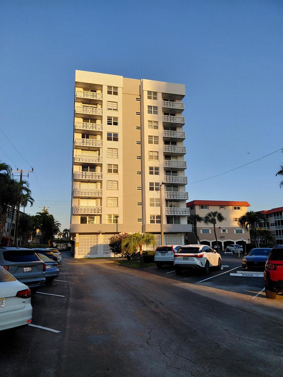 A tall, multi-story apartment building stands behind a parking lot filled with various cars — 3113 S Ocean Drive # 504, Hallandale Beach FL 33009, HALLANDALE BEACH, FL