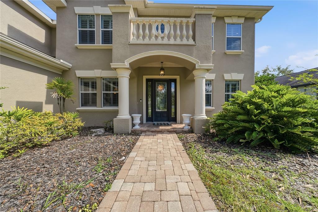 A two-story house exterior features a stone walkway leading to a columned entryway and balcony — 9244 RHEA DRIVE, ODESSA, FL