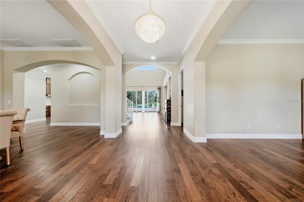 A spacious room with hardwood floors, arched entryways, and a view of a backyard pool — 9244 RHEA DRIVE, ODESSA, FL