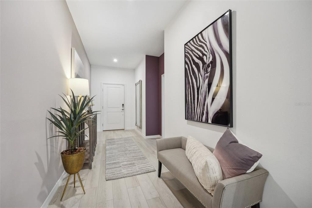 A bright entryway features light wood flooring, a zebra print wall art, and a gray bench — 9225 HARRIS HAWK DRIVE, LEESBURG, FL