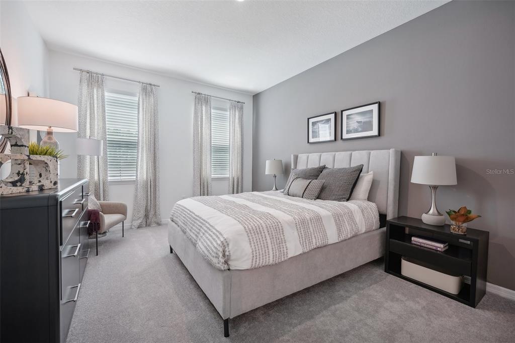 A bedroom features a gray upholstered bed, a black dresser, and two windows with curtains — 9225 HARRIS HAWK DRIVE, LEESBURG, FL
