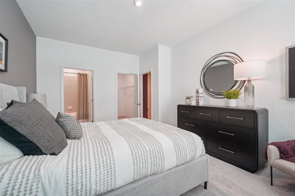 A bedroom features a bed with a textured comforter, a dark dresser, and an attached bathroom — 9225 HARRIS HAWK DRIVE, LEESBURG, FL