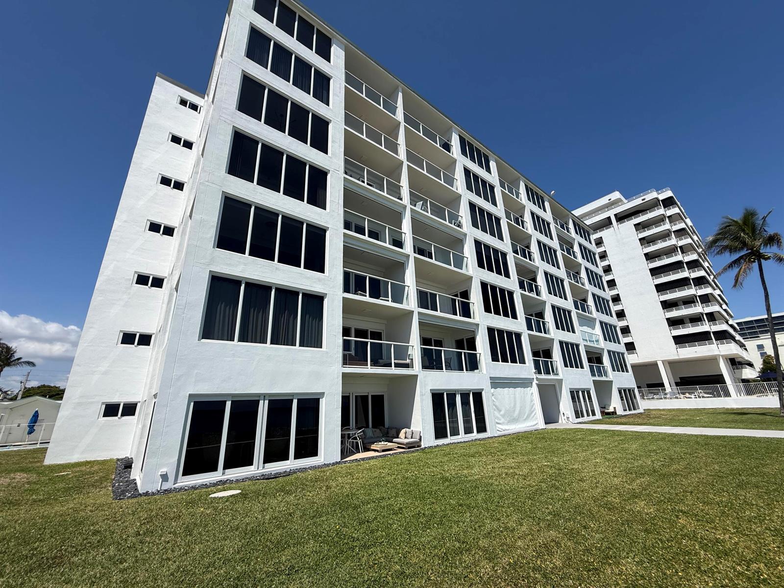 A low-angle exterior view of a white multi-story apartment building with balconies and lawns — 2909 S Ocean Boulevard, Highland Beach FL 33487, HIGHLAND BEACH, FL
