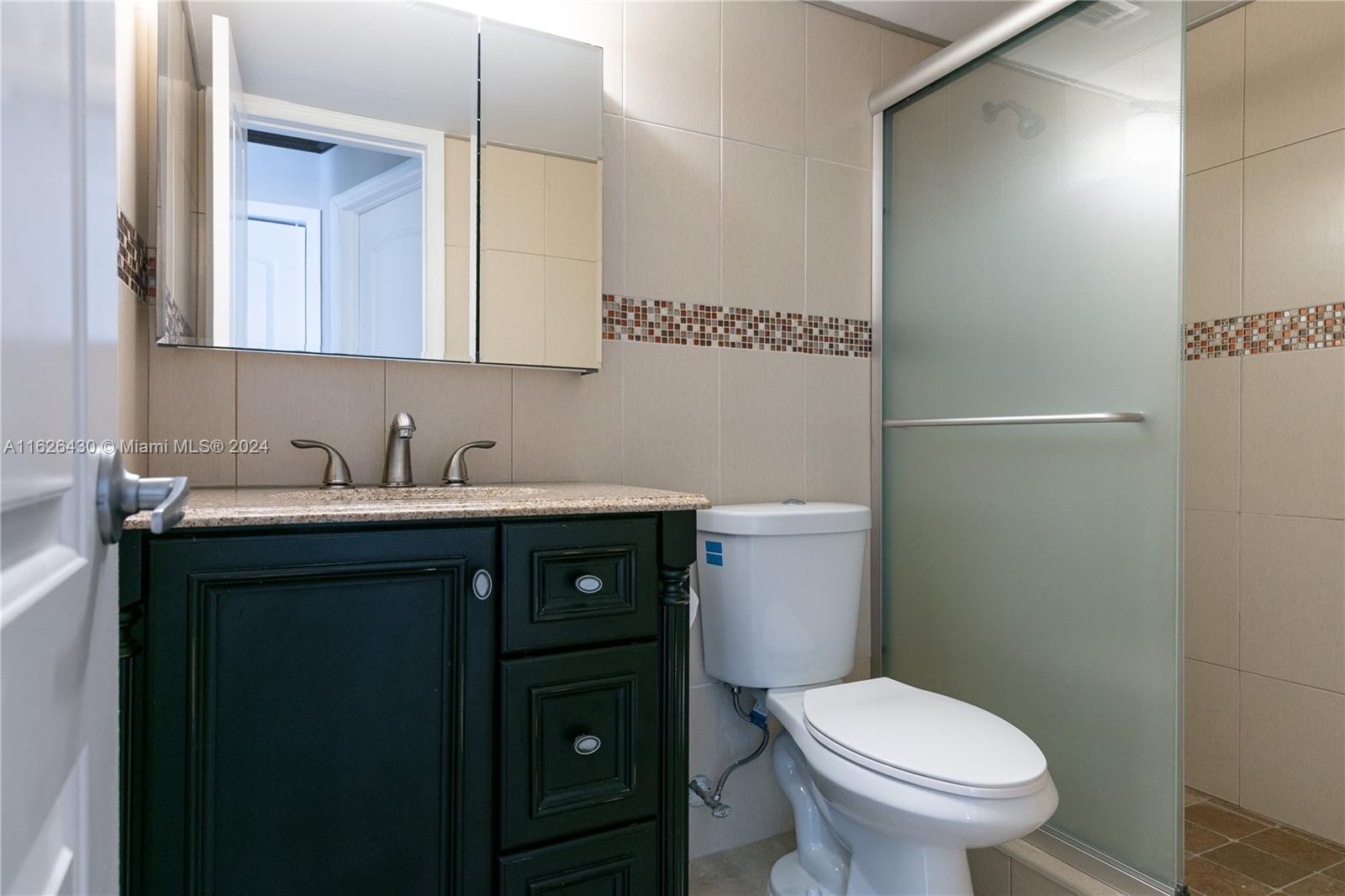 A bathroom features a dark vanity, granite countertop, white toilet, and a glass-enclosed shower — 3135 S Ocean Dr # 227, Hallandale Beach FL 33009, HALLANDALE BEACH, FL