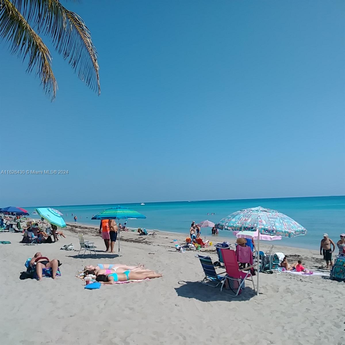 People relax on a sandy beach under colorful umbrellas near the turquoise ocean — 3135 S Ocean Dr # 227, Hallandale Beach FL 33009, HALLANDALE BEACH, FL