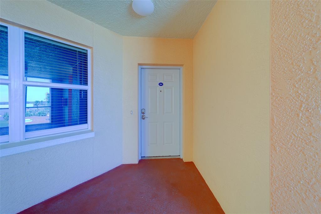 A white front door is centered on a covered balcony with orange flooring and walls — 16450 GULF BOULEVARD UNIT 564, NORTH REDINGTON BEACH, FL
