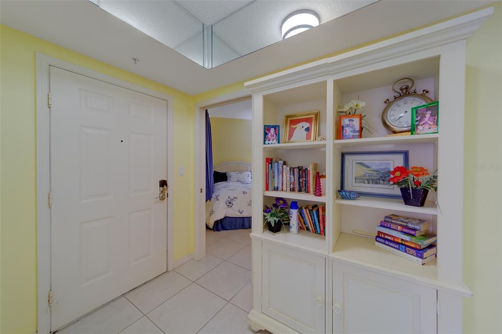 A white bookshelf stands in a tiled entryway next to a door and bedroom doorway — 16450 GULF BOULEVARD UNIT 564, NORTH REDINGTON BEACH, FL