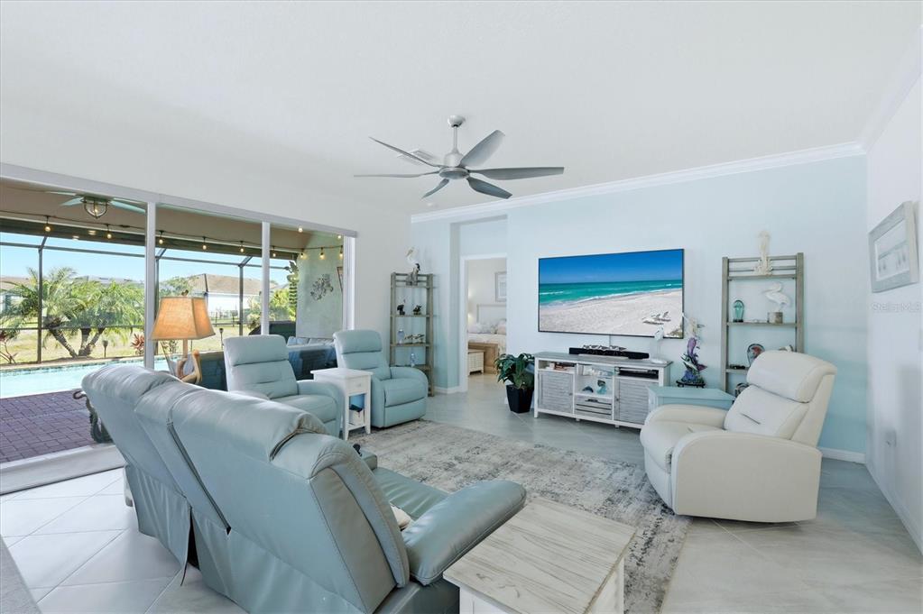 A living room features light blue walls, a ceiling fan, and a view of a pool — 15025 SPANISH POINT DRIVE, PORT CHARLOTTE, FL
