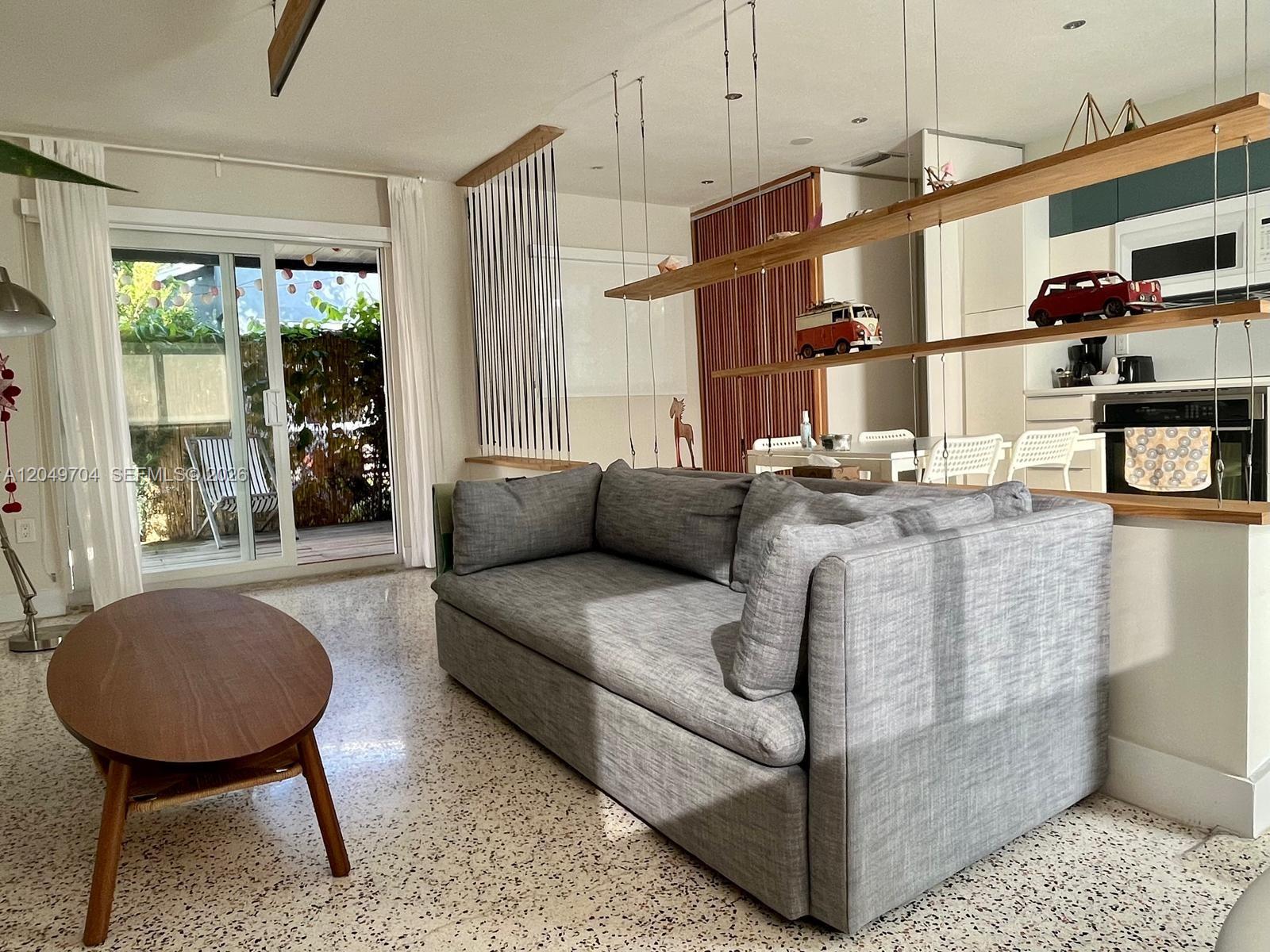 A living room features a suspended wooden shelving unit, a television, and mid-century modern decor — 451 SW 24th Rd # 2, Miami FL 33129, MIAMI, FL