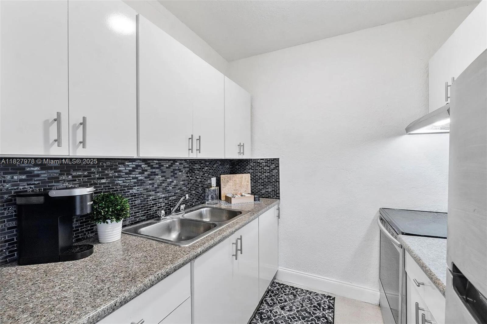 A kitchen features white cabinets, granite countertops, a double sink, and a black tiled backsplash — 1401 NW 103rd St # 139, Miami FL 33147, MIAMI, FL