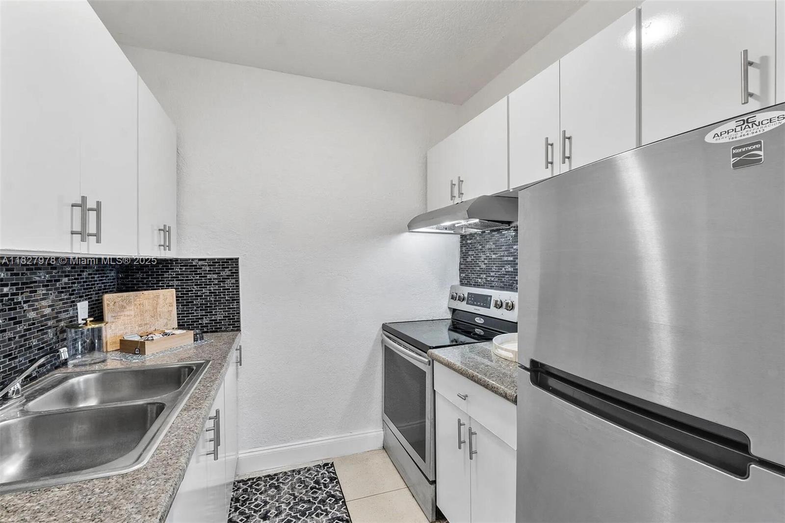 A galley kitchen features white cabinets, granite countertops, stainless steel appliances, and a black backsplash — 1401 NW 103rd St # 139, Miami FL 33147, MIAMI, FL