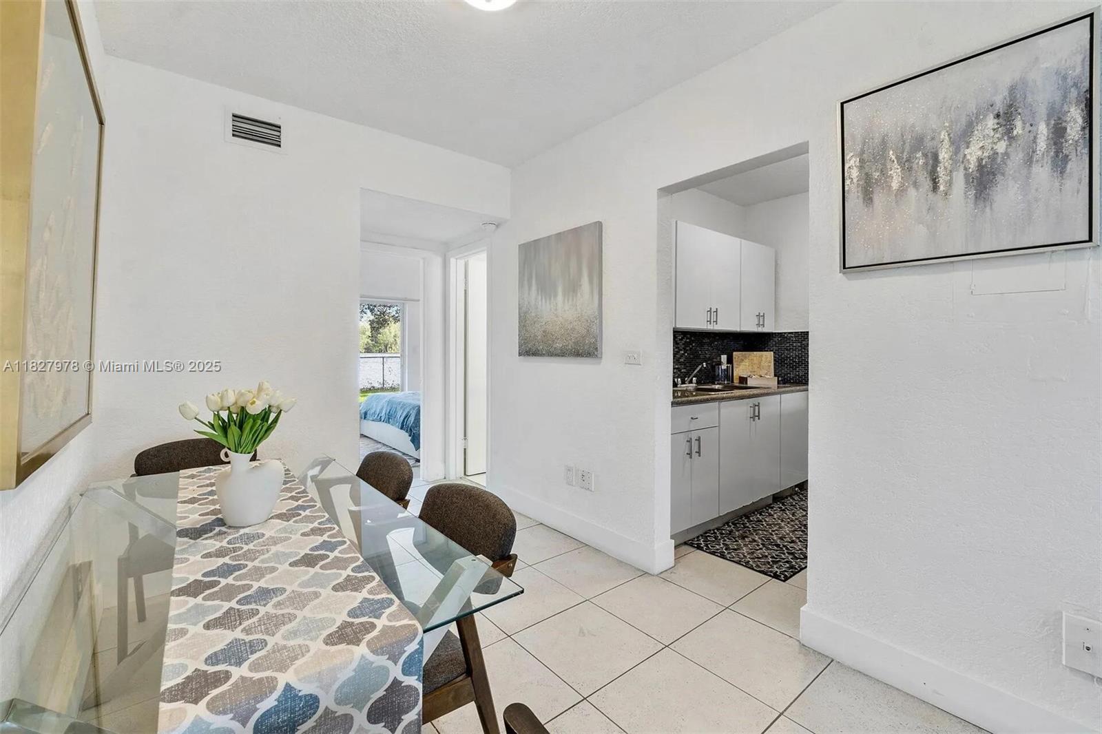 A dining area with a glass table leads to a kitchen and a bedroom beyond — 1401 NW 103rd St # 139, Miami FL 33147, MIAMI, FL