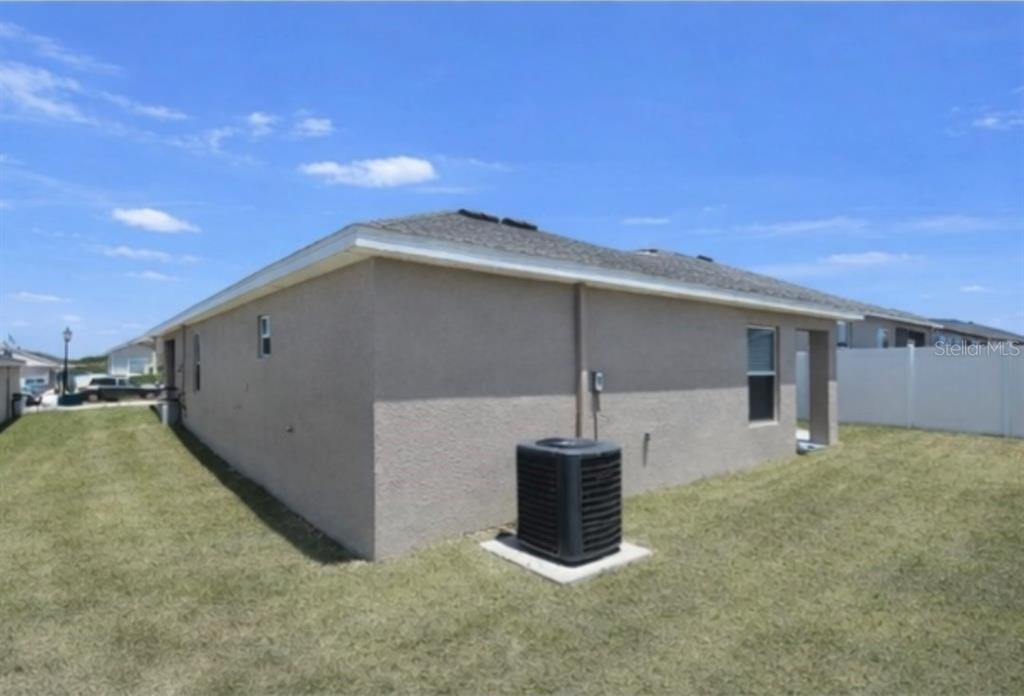 The exterior of a tan stucco house features a gray shingled roof and air conditioner — 1540 FLEUR DRIVE, DAVENPORT, FL
