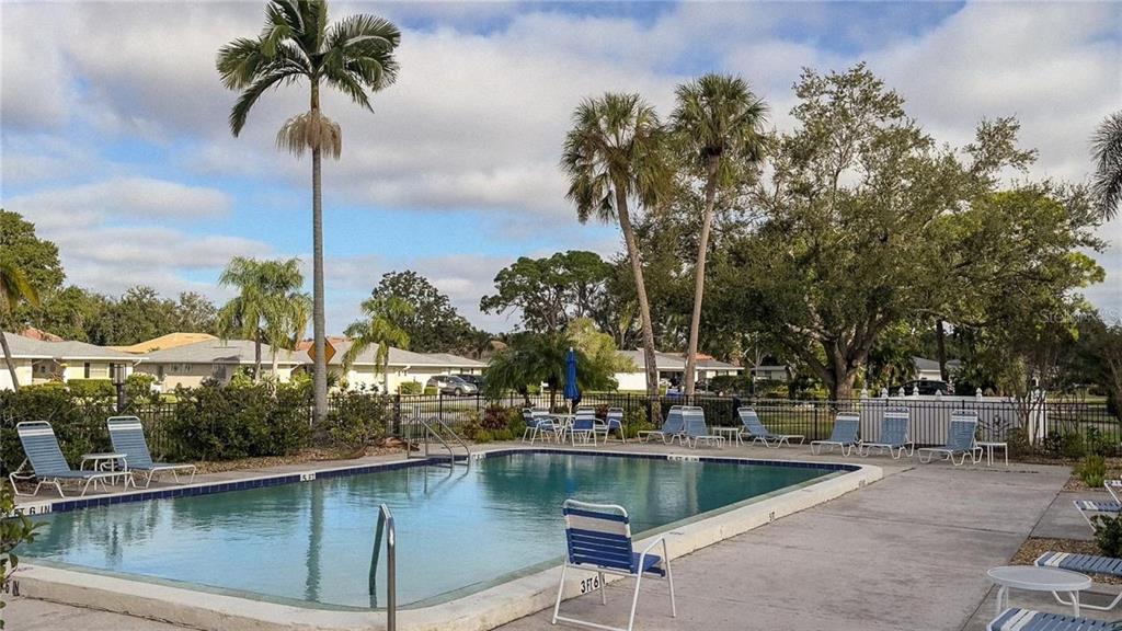 An outdoor swimming pool surrounded by lounge chairs, palm trees, and a black metal fence — 7461 W COUNTRY CLUB DRIVE N UNIT 306, SARASOTA, FL